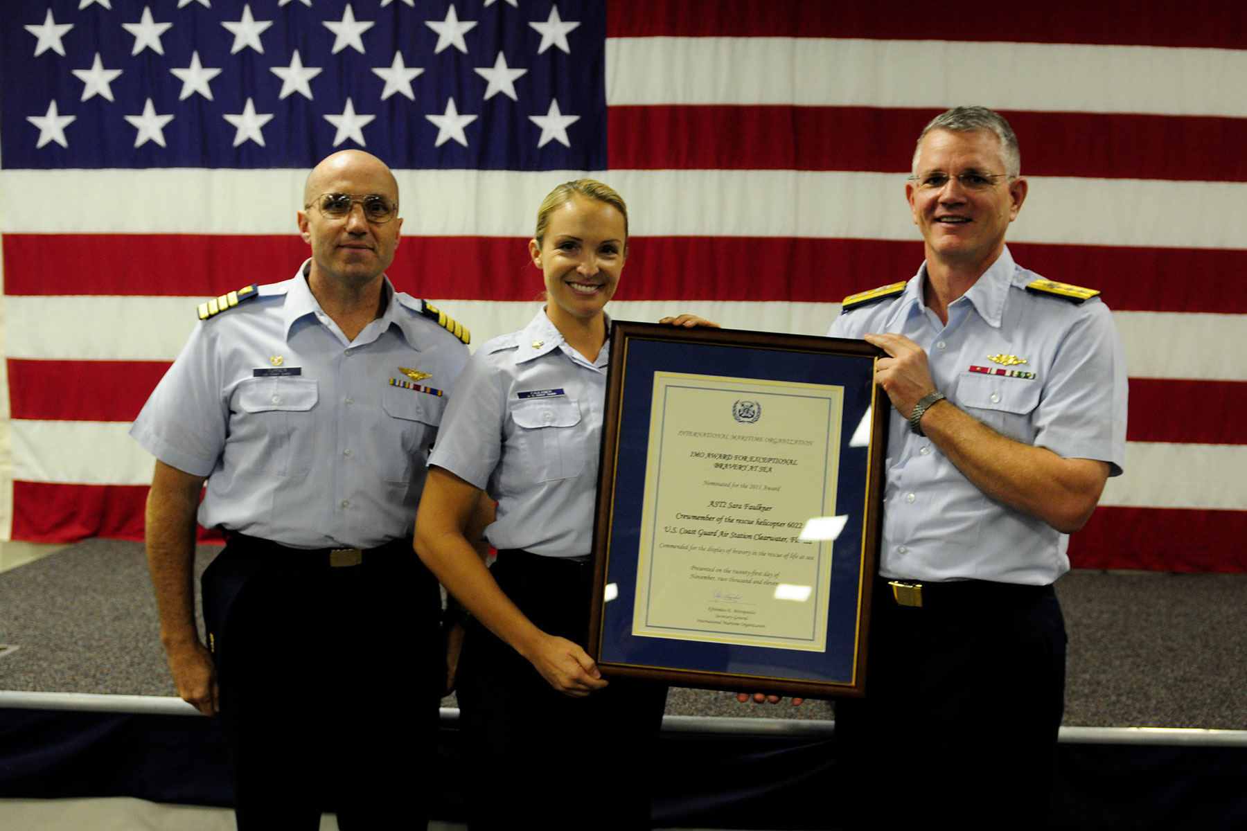 Coast Guard Petty Officer 2nd Class Sara Faulkner, receives recognition from Rear Admiral Bill Baumgartner, Commander of the 7th Coast Guard District and Capt. John Turner, commanding officer of Air Station Clearwater during an awards ceremony at Air Station Clearwater. (U.S. Coast Guard/Tara Molle)